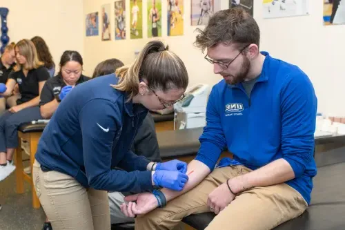 An athletic training student practices closing a wound on another student